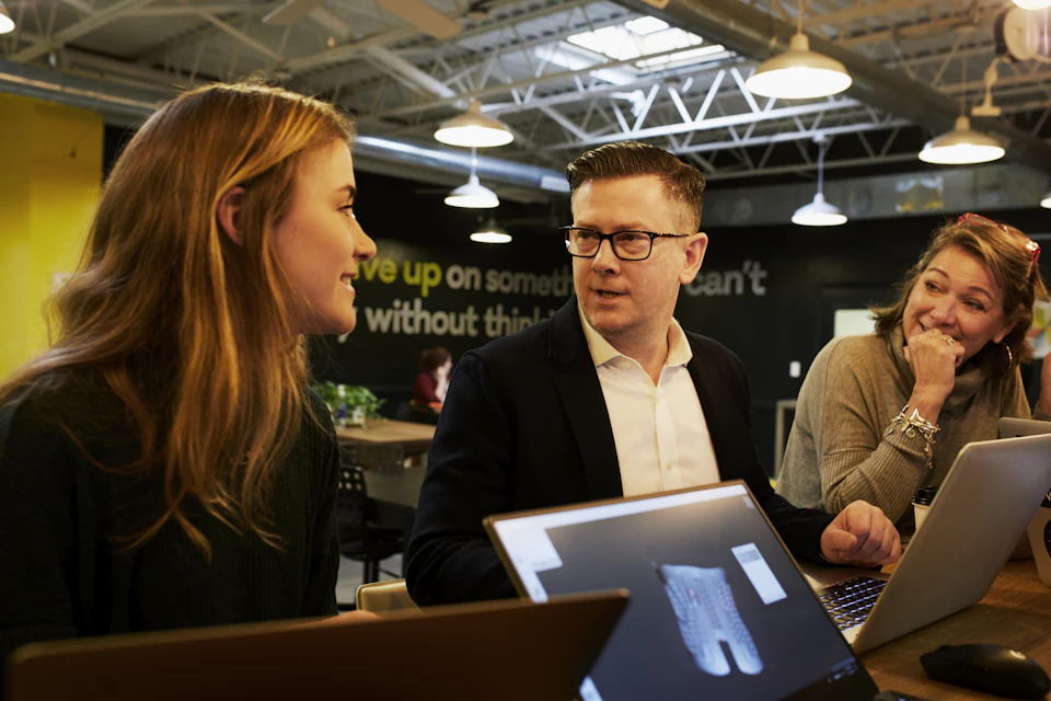 Three colleagues discussing work around a table; illustrative stock photography