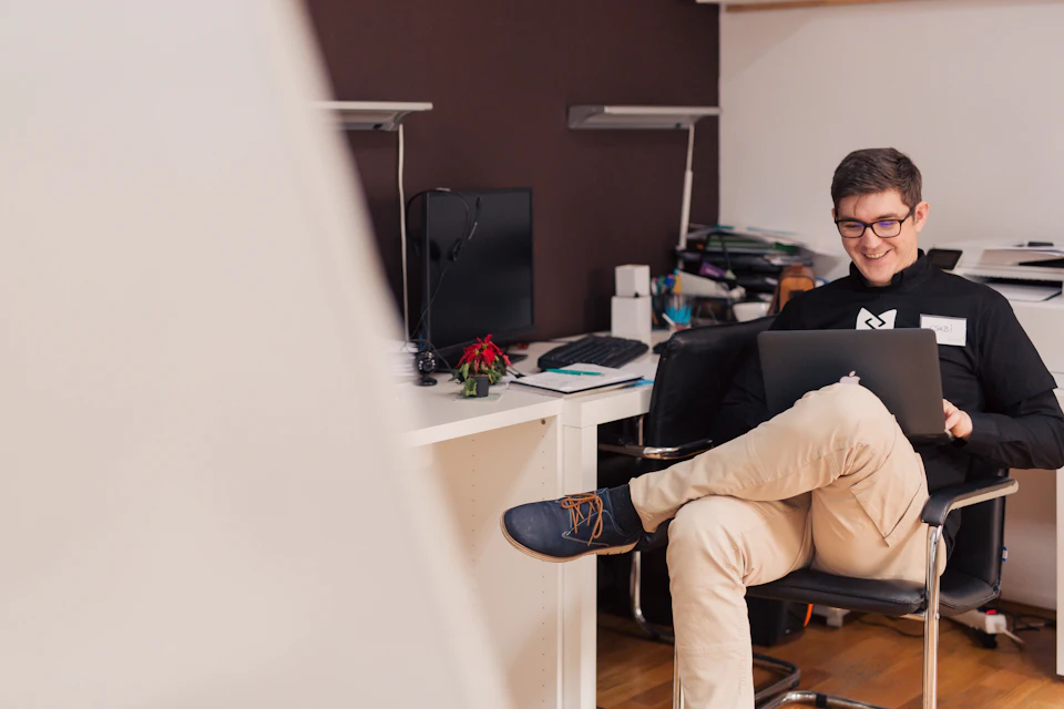 A smiling man with glasses working on a laptop in an office; illustrative stock photography