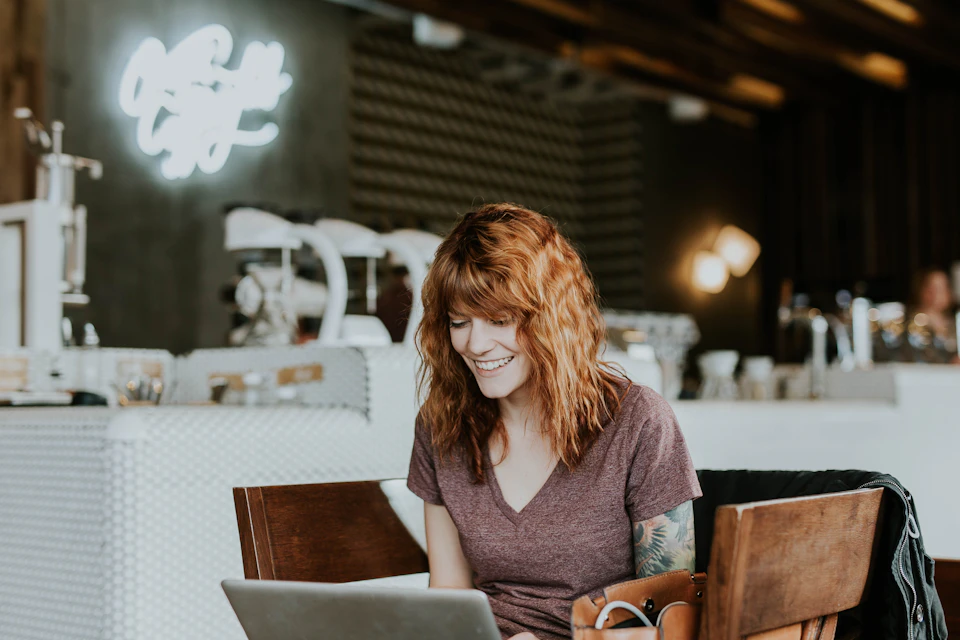 A smiling woman writing on a laptop in a cafe; illustrative stock photography
